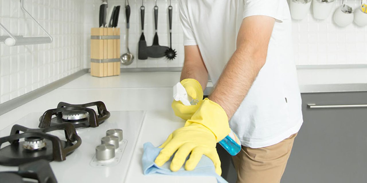 Young serious man wearing rubber yellow gloves cleaning the stov